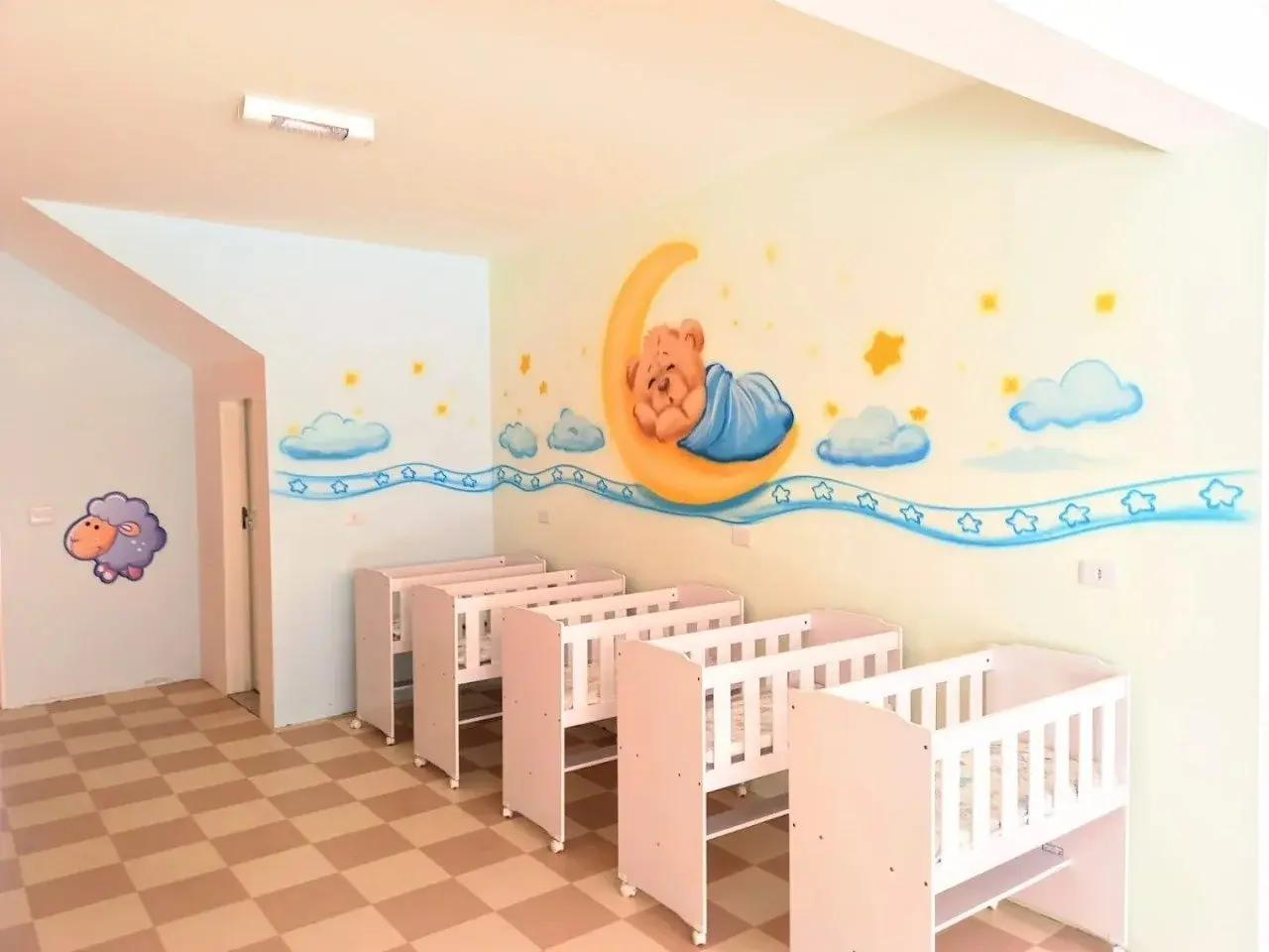Dormitório do berçário com berços individuais e decoração de ursinho na parede, Unidade Santo Antônio, Osasco.