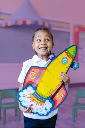 Aluna sorrindo segurando um foguete de papelão colorido no Ensino Fundamental I do Colégio Antônio Villas Boas, Osasco.