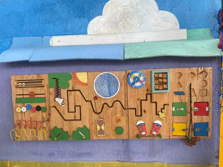 Painel sensorial de madeira para atividades táteis na parede do pátio do Colégio Antônio Villas Boas, Osasco.