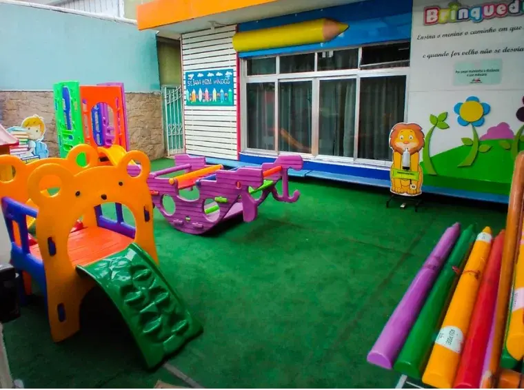 Playground infantil com grama sintética, escorregador e decoração de lápis gigantes na Unidade Ayrosa do Colégio Antônio Villas Boas em Osasco.